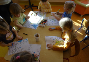 Szóstka dzieci koloruje zaszyfrowane według kodu ilustracje dinozaurów.